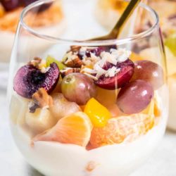 A close up of layered Ambrosia Salad with mandarins, grapes, cherries, pears, and peaches.