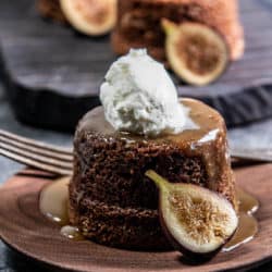 A figgy pudding on a serving plate with whipped cream and a fresh fig.