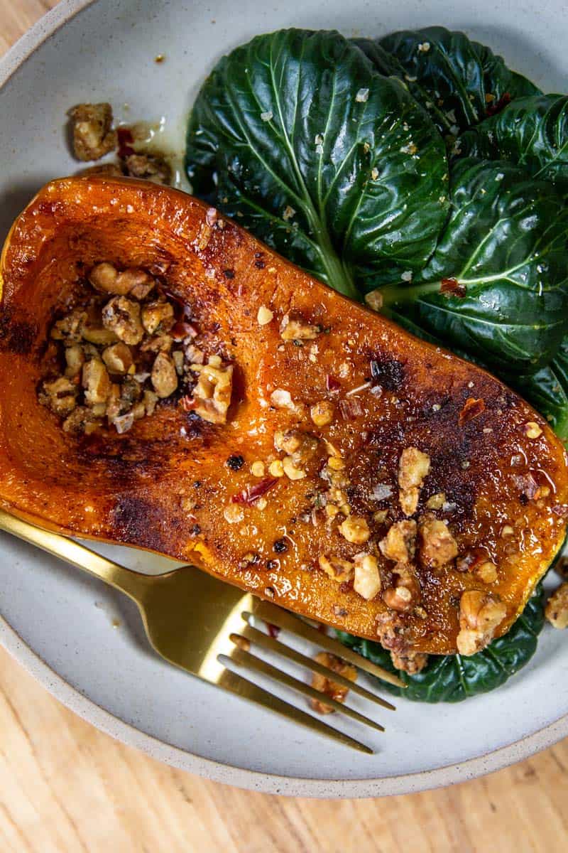 Honeynut squash roasted and plated with walnut and rosemary crumble and leafy greens.