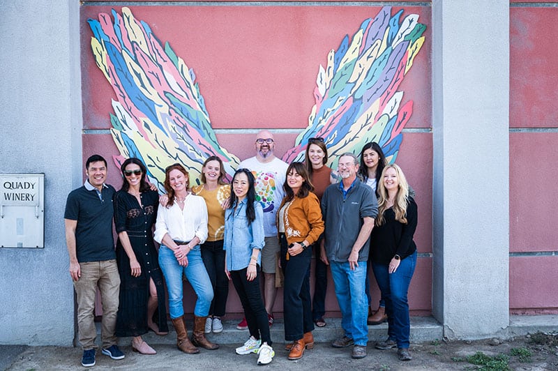 A group of peopl in frint of a mural at Quady winery.