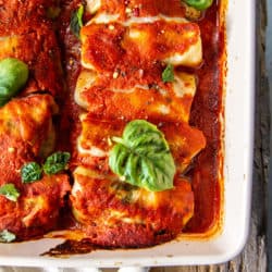 Baked cabbage rolls in red sauce under basil leaves.