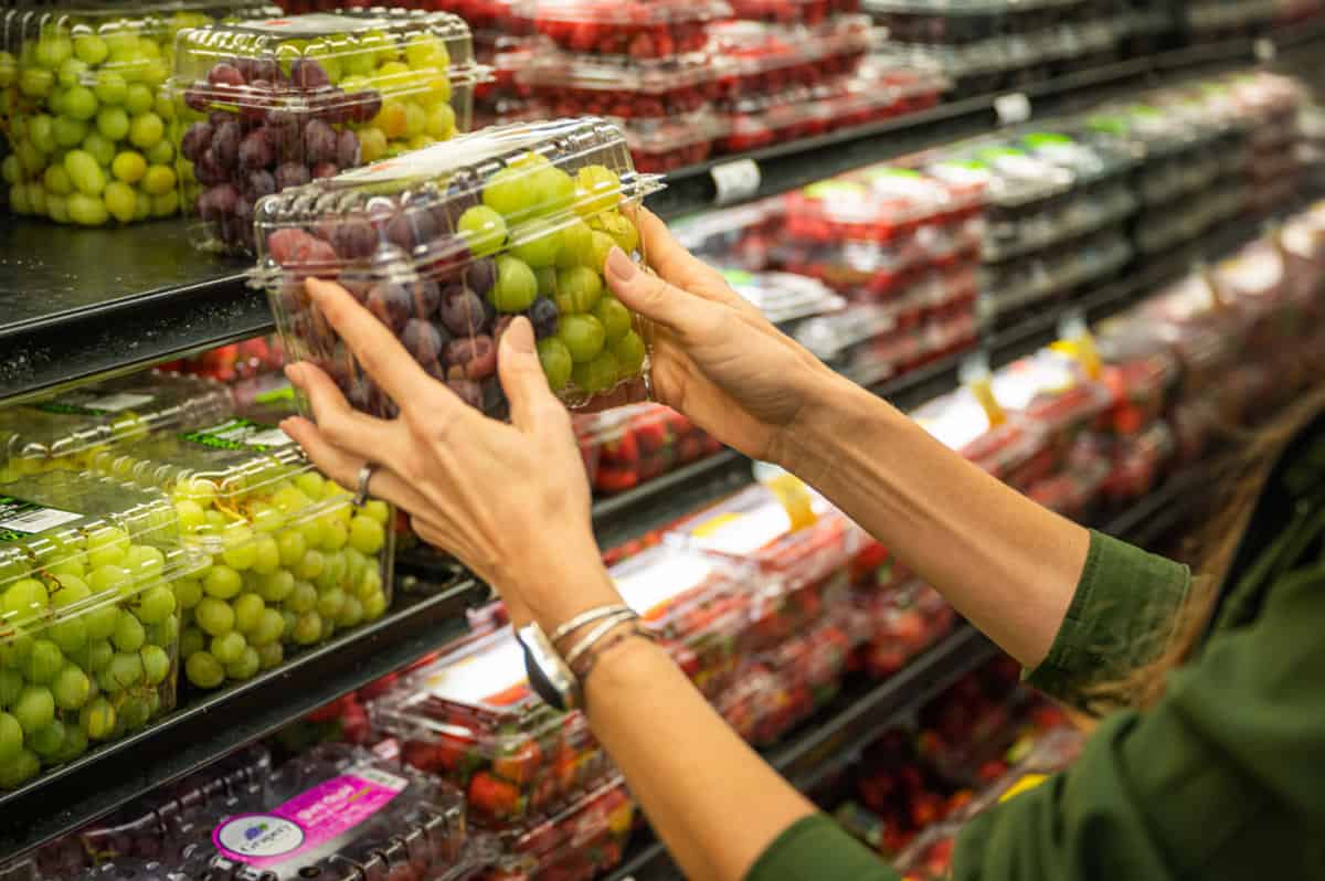 shopper reaching for grapes on grocery store shelf.