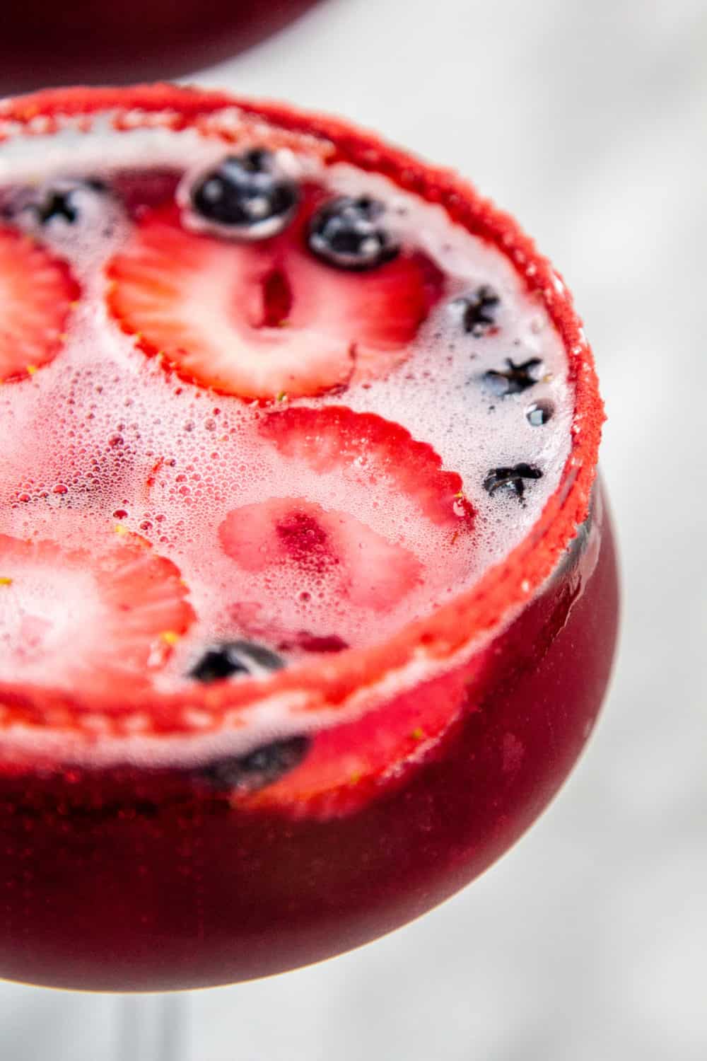 A blueberry cocktail with frozen blueberry and strawberry slices. 