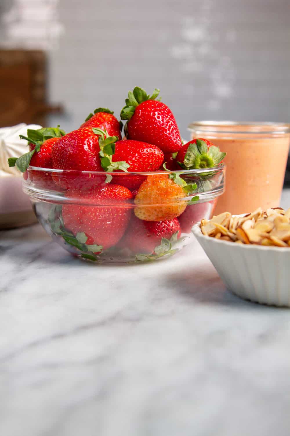 A bowl of strawberries next to a bowl of strawberry curd.