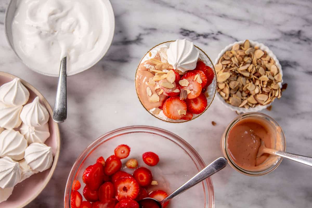 An assembled strawberry eton mess with bowls of the ingredients to make more around it. 