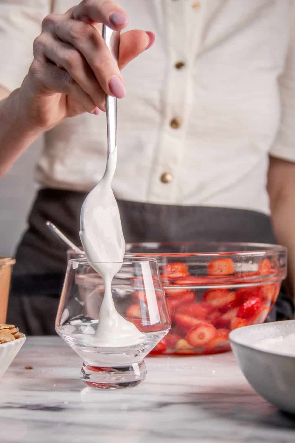Adding whipped cream to a serving glass for eton mess.