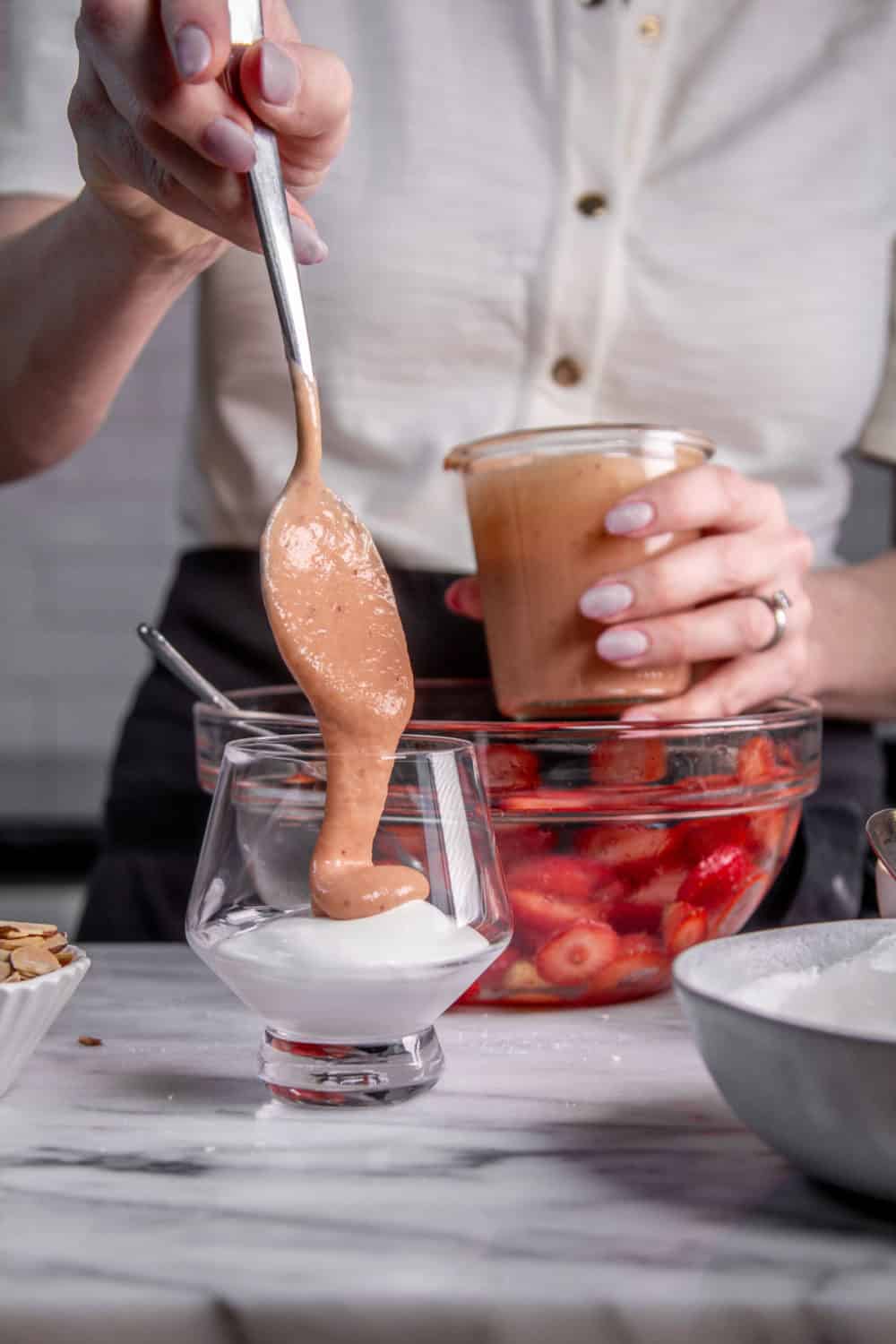 Adding strawberry curd to a glass with whipped cream.