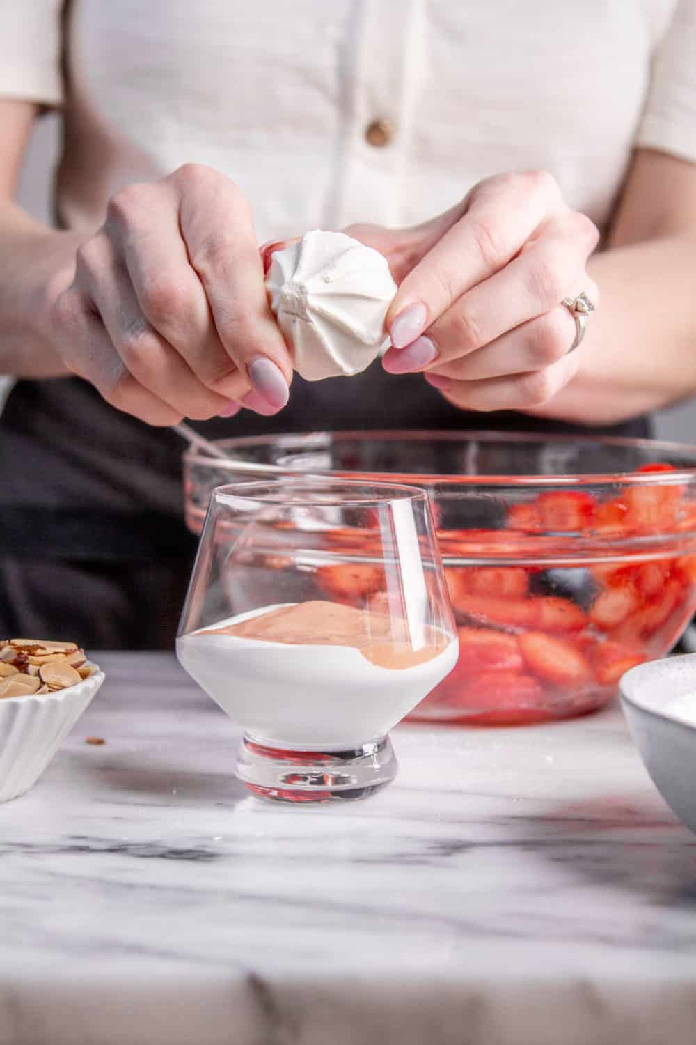 Breaking meringues into a serving glass with strawberry curd and whipped cream.