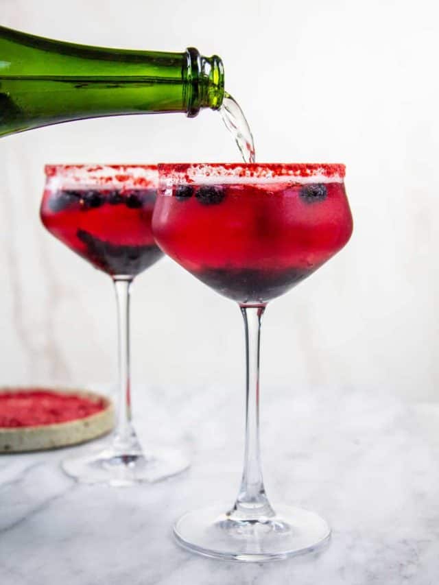 Coupe glasses with a red cockytail and a red rim. Saprkling wine is being poured into the glass.