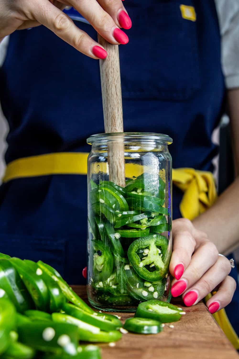 Packing jalapeno slices into jars an depressing them with a wooden spoon handle.