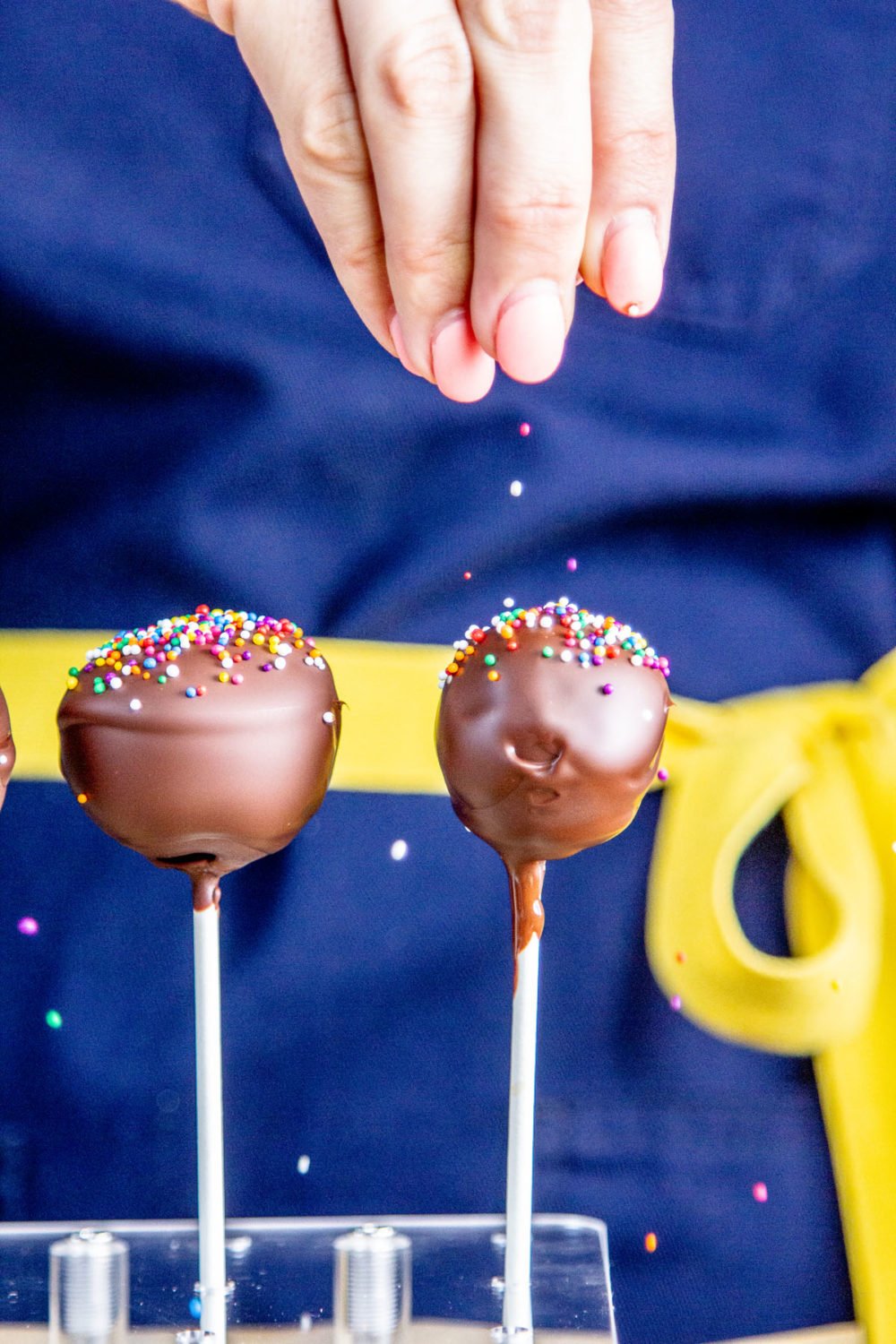 Sprinkles being sprinkled on top of chocolate cake pops.