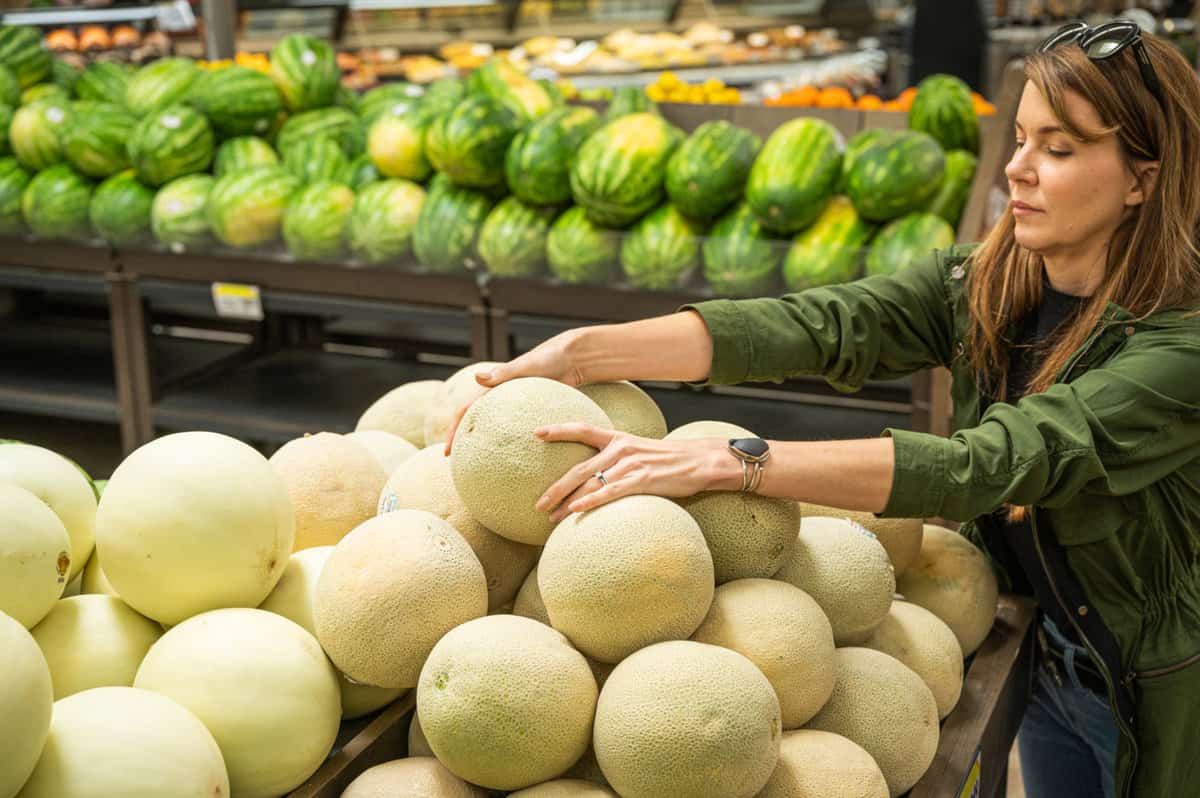 woman grabbing a melon from the grocery store