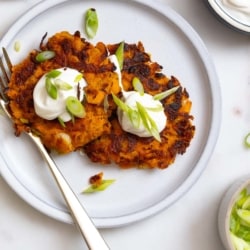 Latke-Inspired Sweet Potato Pancakes topped with sour cream and green onions.
