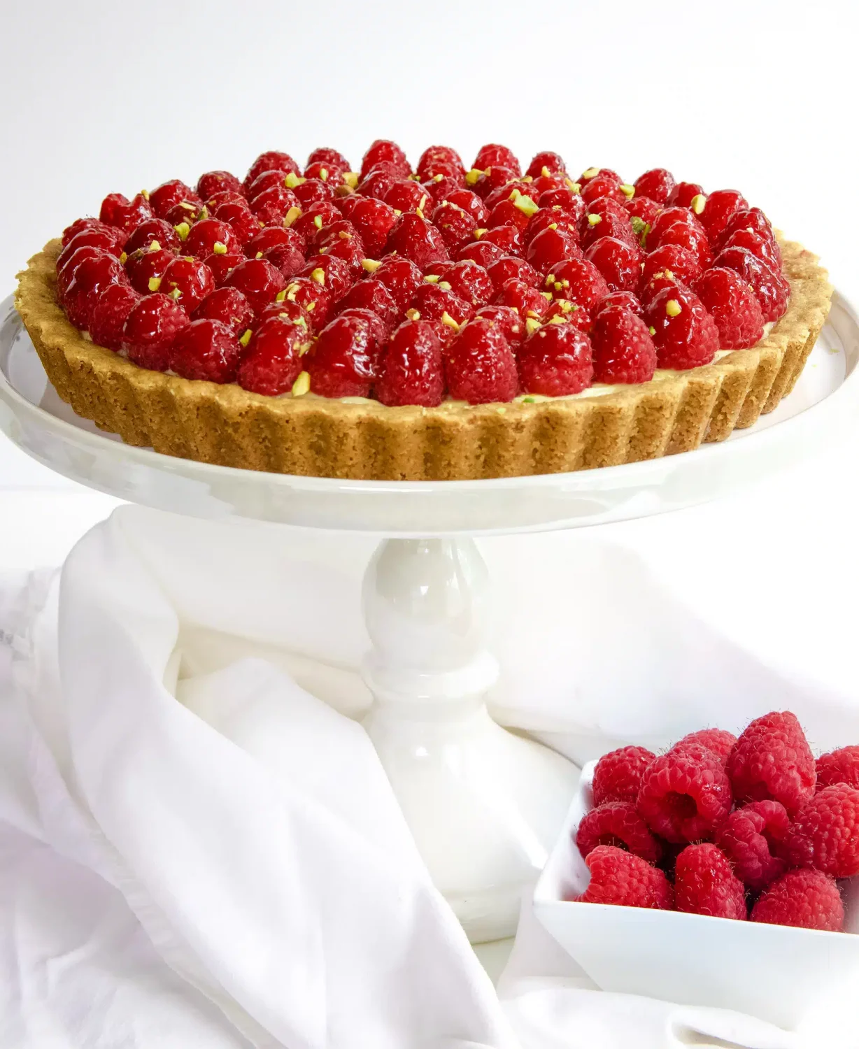Raspberry tart with pistachio crust on a white porcelain pedestal