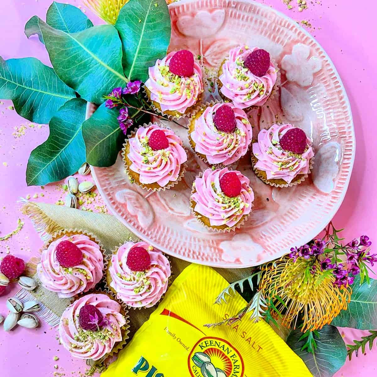 platter of raspberry pistachio cupcakes with flowers and nuts