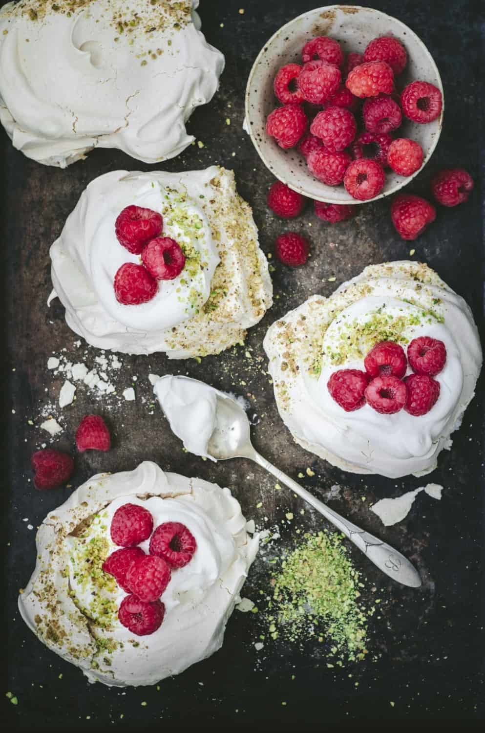Raspberry pistachio pavlovas on a baking sheet
