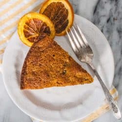 Slice of carrot olive oil cake on a plate with dehydrated orange slices.