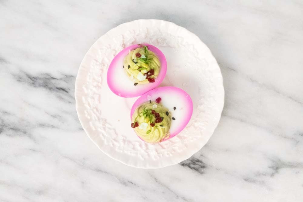 Two pink deviled eggs on a serving plate.