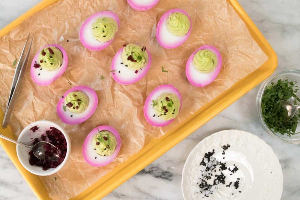 Garnishing pink-hued deviled eggs with light green filling.