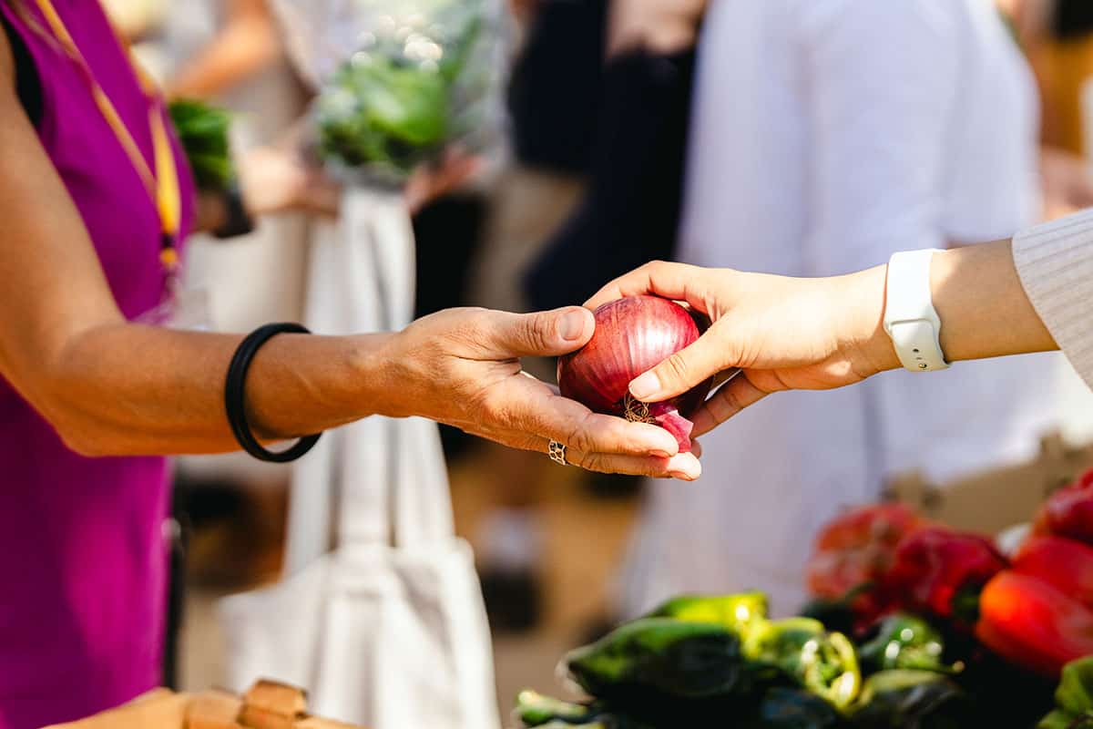 people handing each other a red onion at a farmers market
