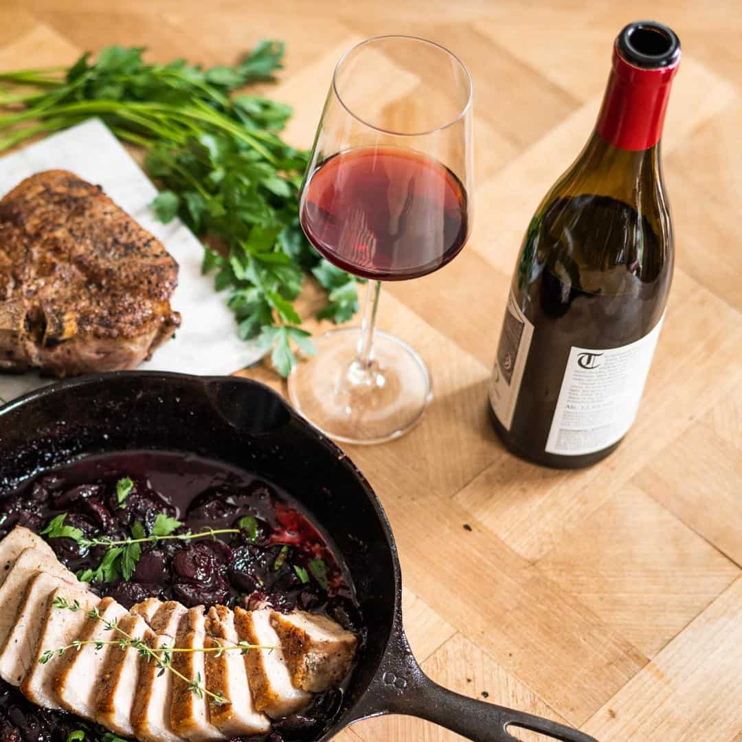 Birichino Cinsault in a bottle with a glass poured and pork sliced in a cast iron pan