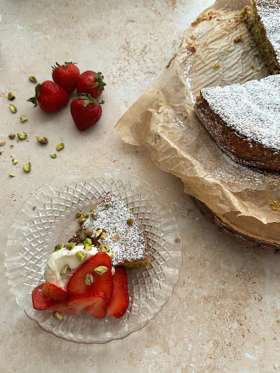 slice of pistachio cake on a glass plate topped with strawberries and mascarpone