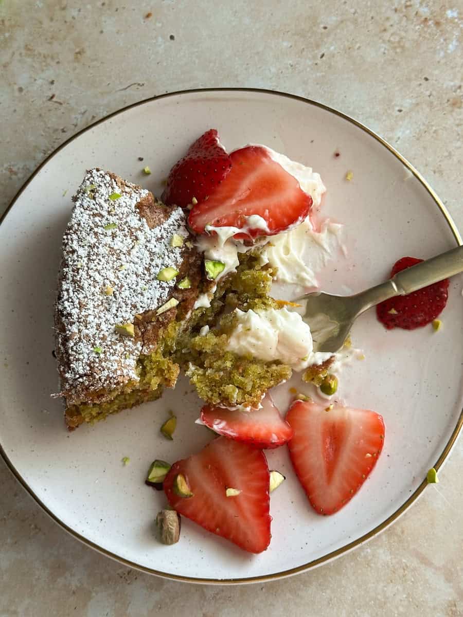 pistachio cake on a white plate topped with macerated strawberries and mascarpone 