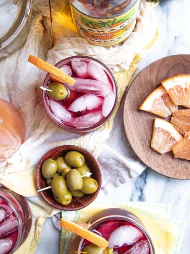 Top down look into glasses of Golden State Lambrusco Spritz and small plates of garnishes.