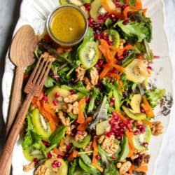 A platter of kiwi salad with leafy greens, kiwi slices, walnuts, dried apricots, and pomegranate.