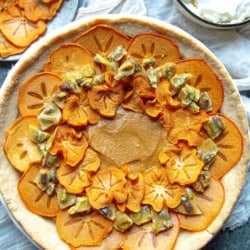 A close up of a persimmon pie decorated with crispy dehydrated persimmons and pistachio brittle.