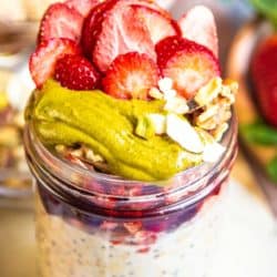 A close up of nutty overnight oats toppings. Pistachio butter, strawberry jam, and sliced strawberries.