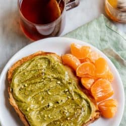 Toast with pistachio butter & honey and mandarins next to a cup of hot tea.