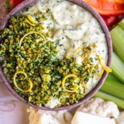 Close up of a bowl of tzatziki garnished with with gremolata and served with crudite.