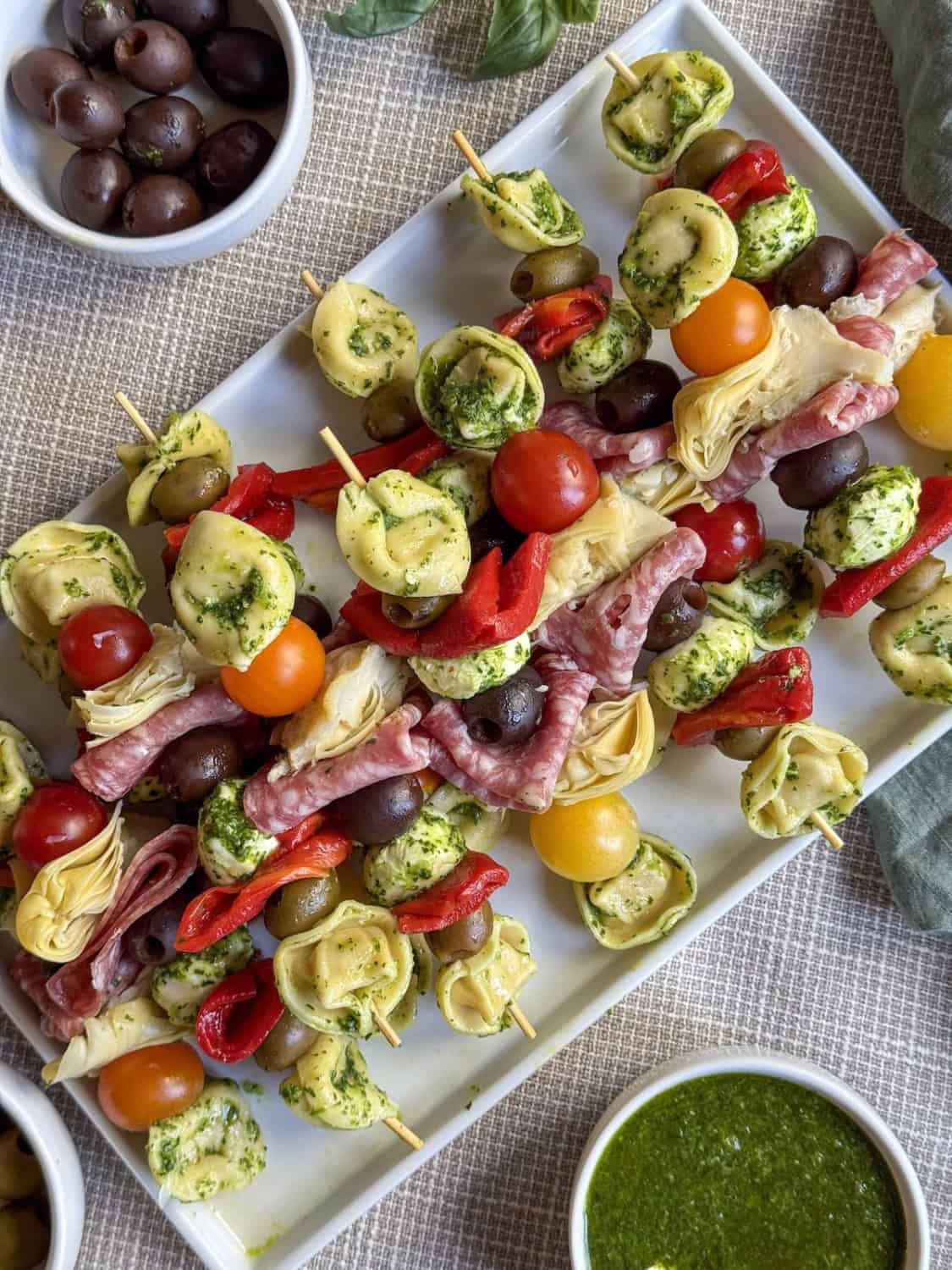 antipasto skewers on a white platter with a variety of sauces