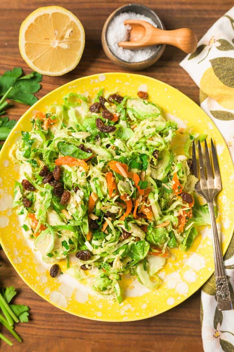 Shaved Brussels Sprouts salad on a yellow serving plate with dried fruit.