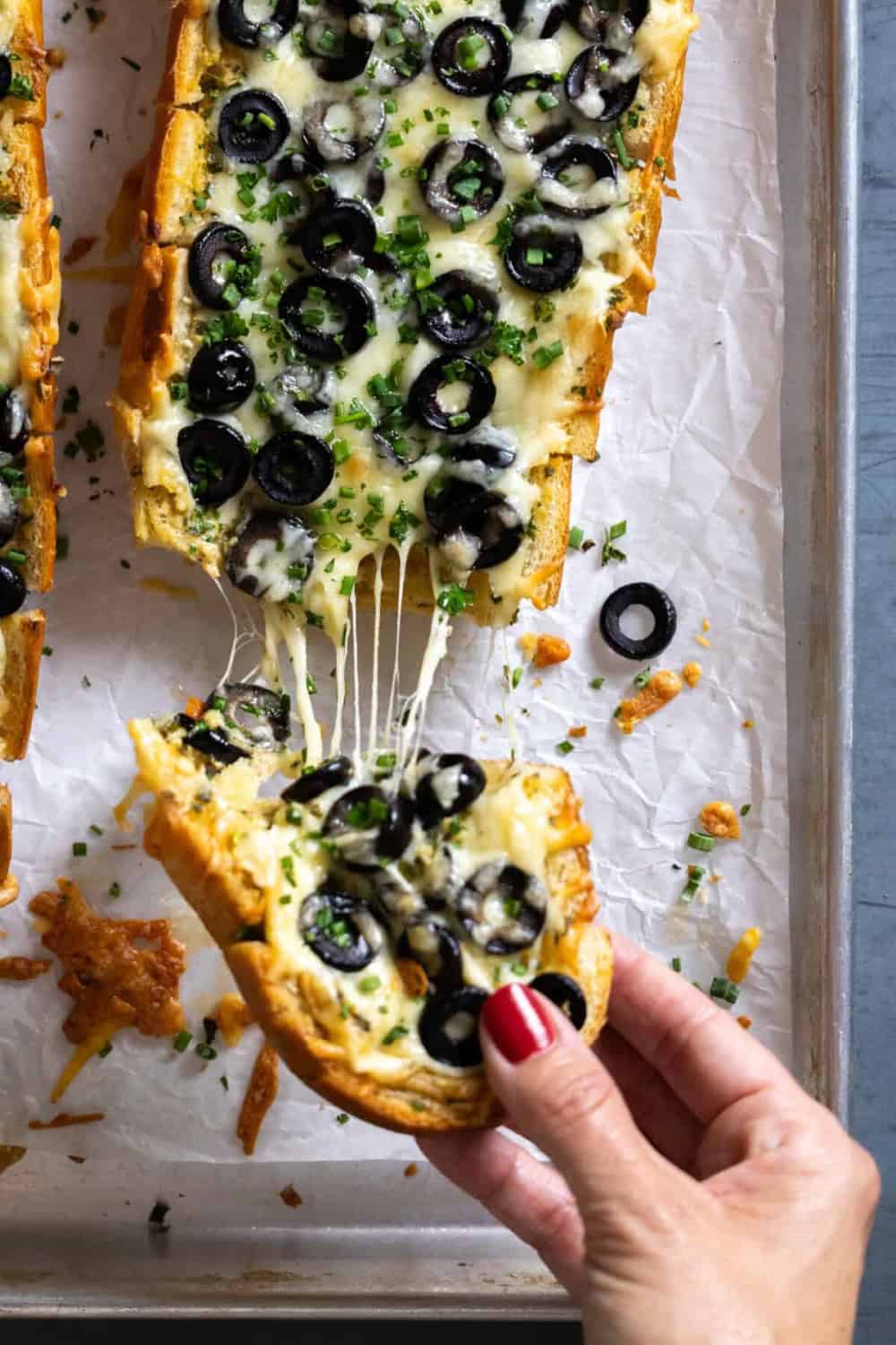 woman pulling a slice of cheesy olive topped garlic bread