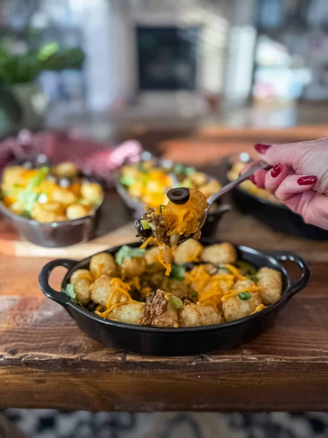 woman taking a bite of a cheesy tater tot casserole in black dish