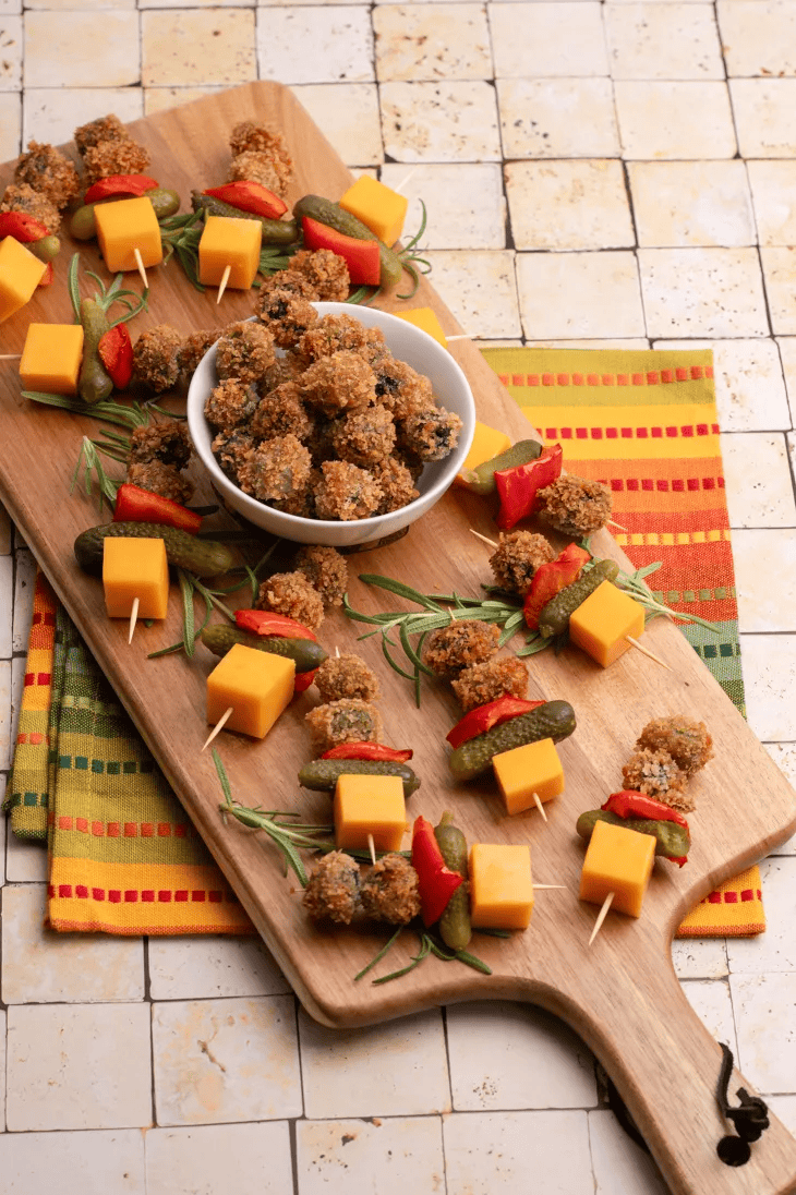 fried olives on a skewer with cheese and pickles arranged on a wooden board