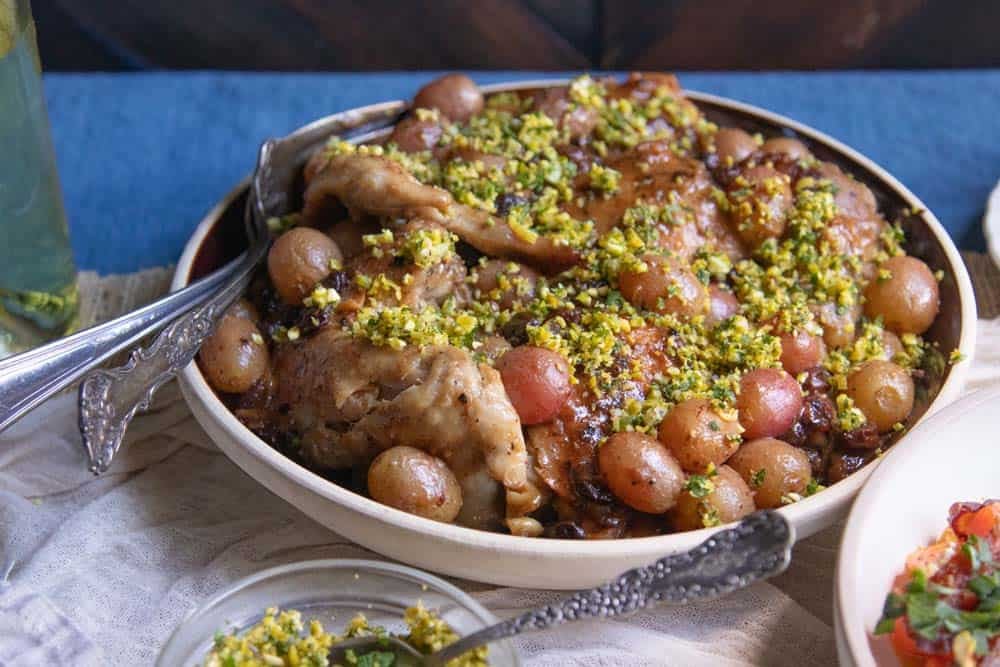 Close up from side of a chicken recipe with wine, grapes, and raisins garnished with pistachio gremolata.