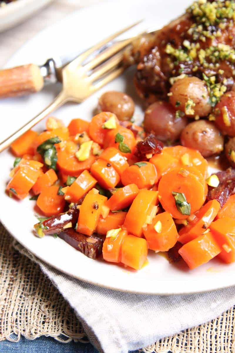 Close up of Honey Butter-Glazed Carrots garnished with basil, pistachios, and dates.