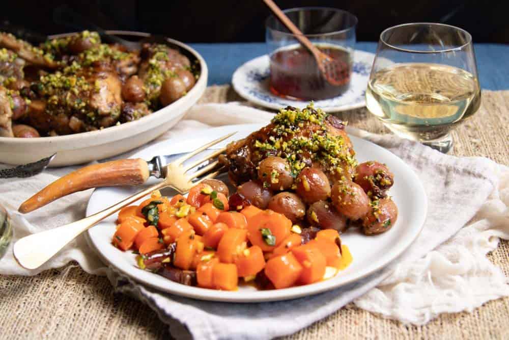 A plate with some of the chicken, cooked grapes and pan sauce as well as a serving of honey glazed carrots.