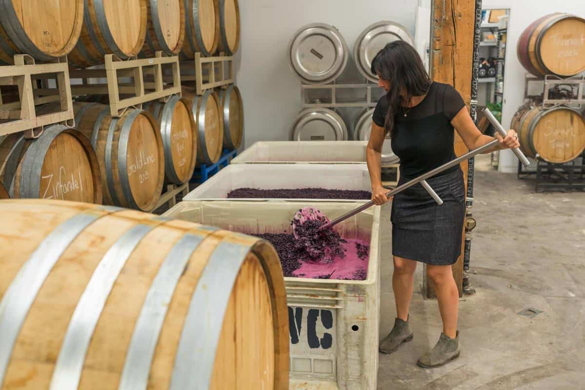 woman punches down winegrapes in large container