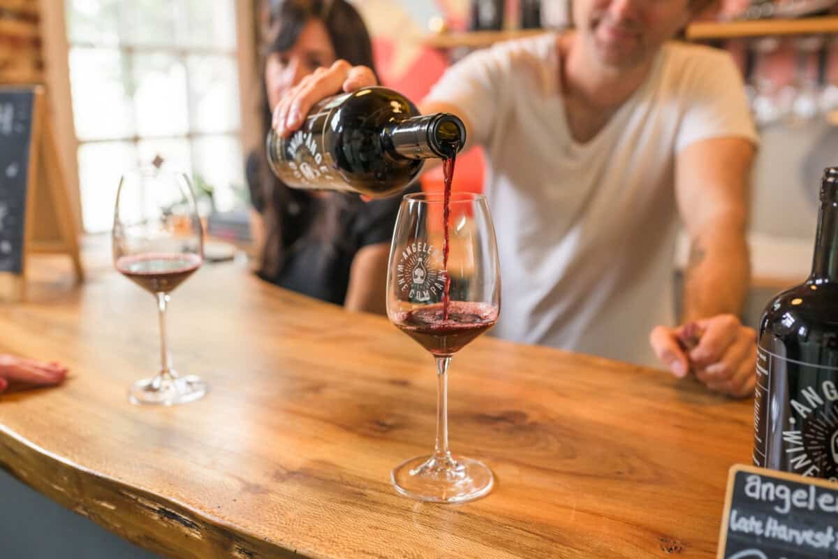 man pouring wine into glass on a wooden counter