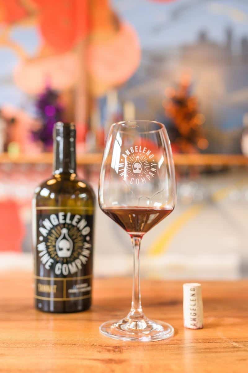 red wine in a glass next to a bottle of wine on a wooden counter