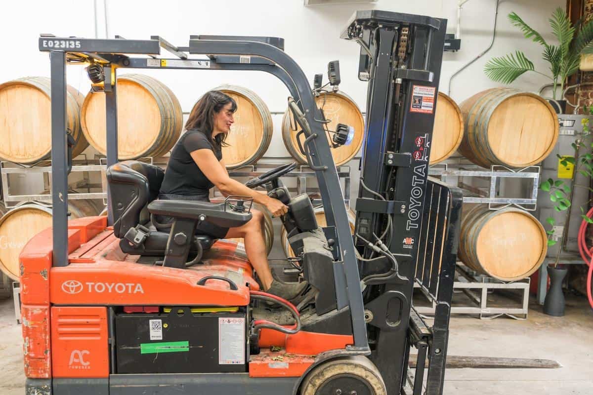 woman drives tractor inside winemaking warehouse