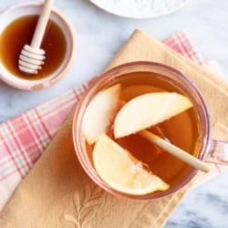 Close up of a glass of jujube tea with lemon and apple slices.