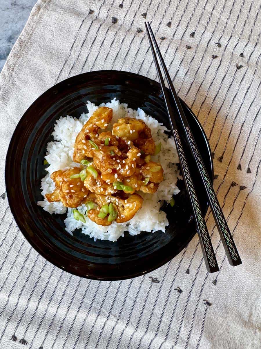 A zoomed out imag of a black bowl filled with white rice and orange cauliflower.
