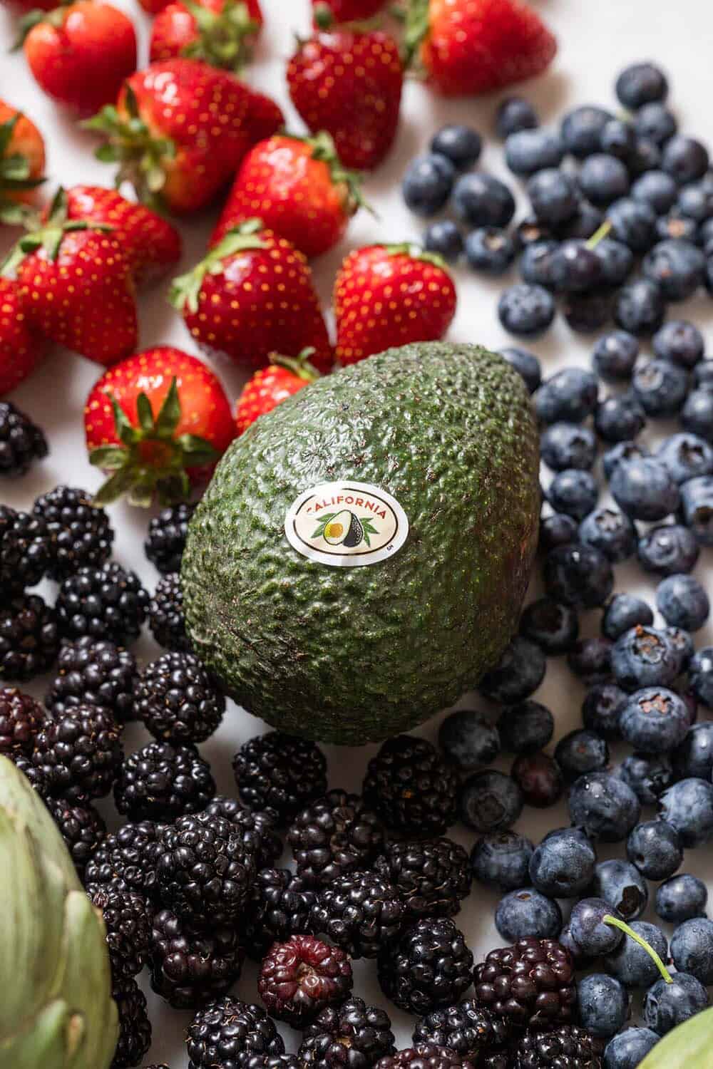 An avocado with a sticker on it surrounded by fresh berries.