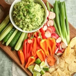 Chips, guac, and crudites on a wooden serving board.