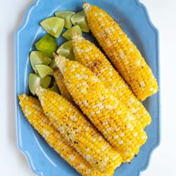 Ears of corn and lime wedges on a blue serving platter.